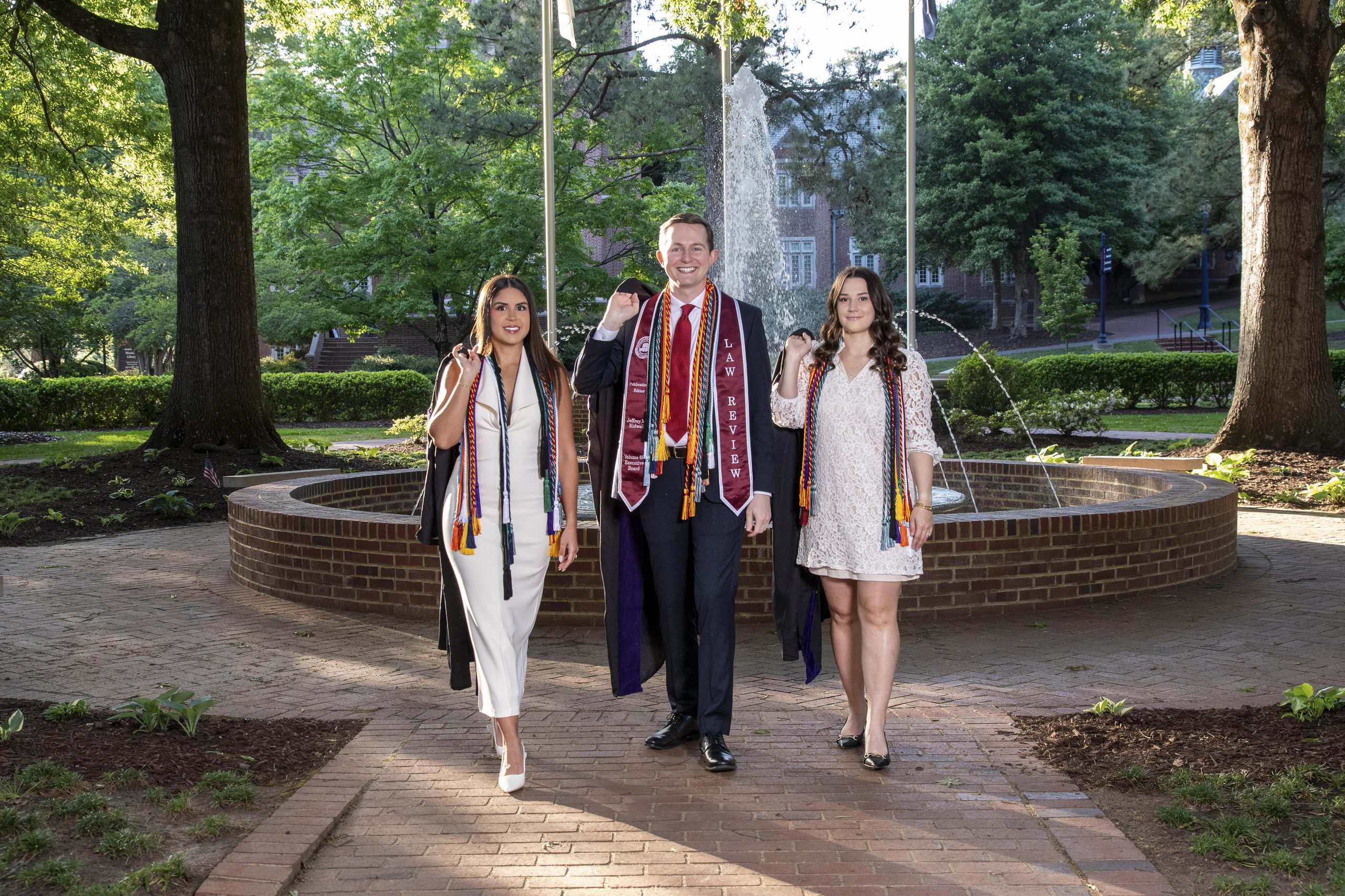 Graduate in a stole walking with family past a garden fountain