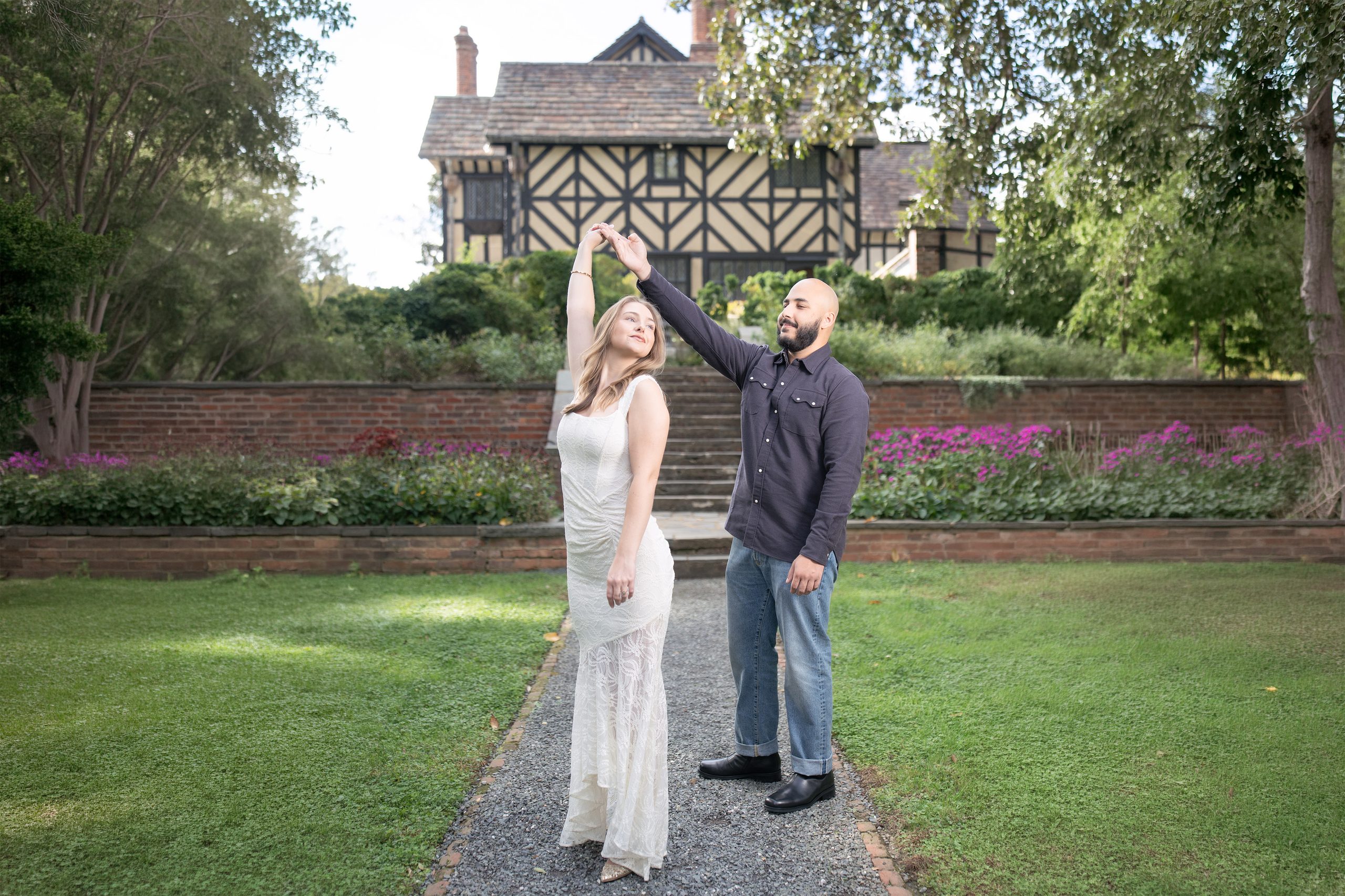 Engaged couple celebrating on a garden path outside a Tudor-style manor