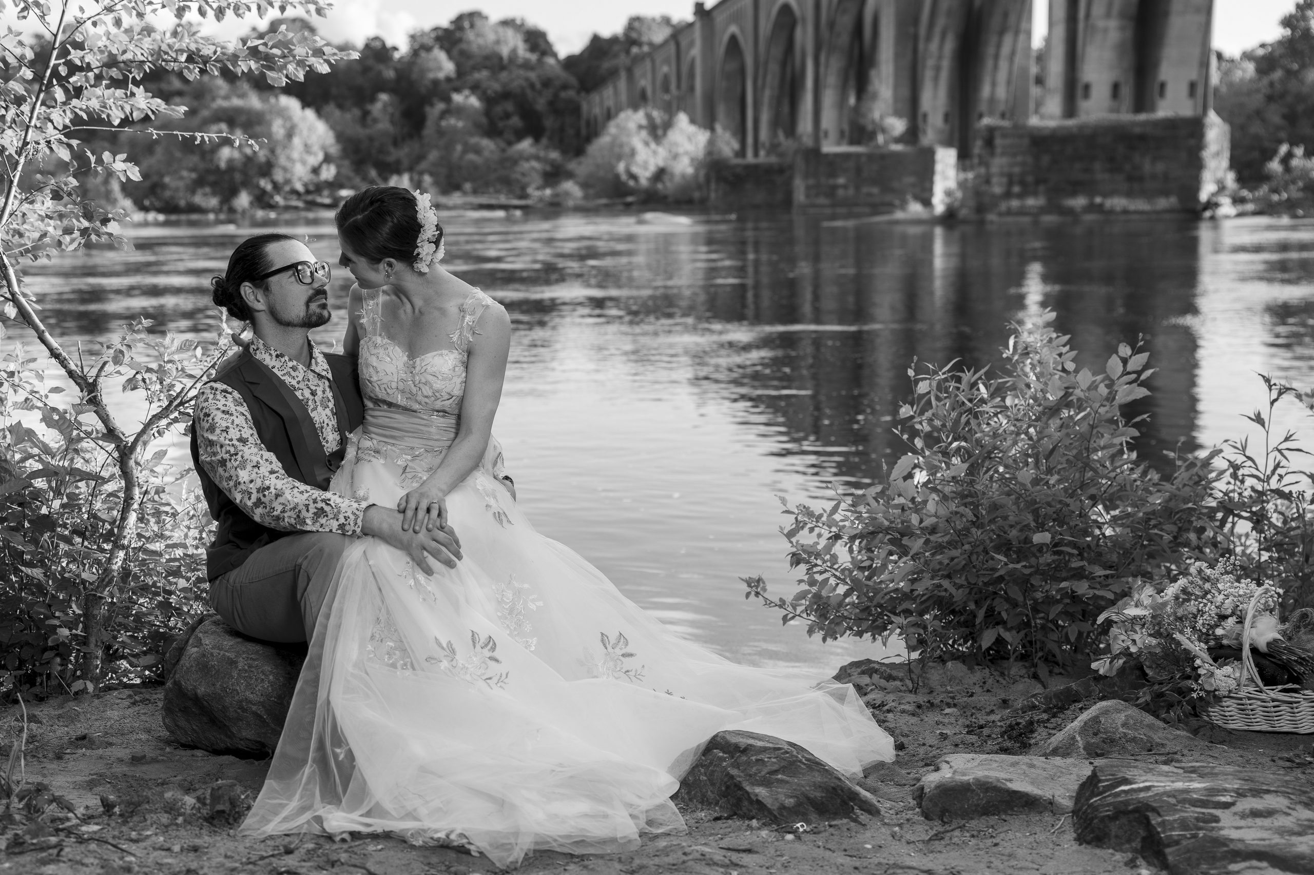 Black-and-white portrait of a bride and groom seated beside a garden pond