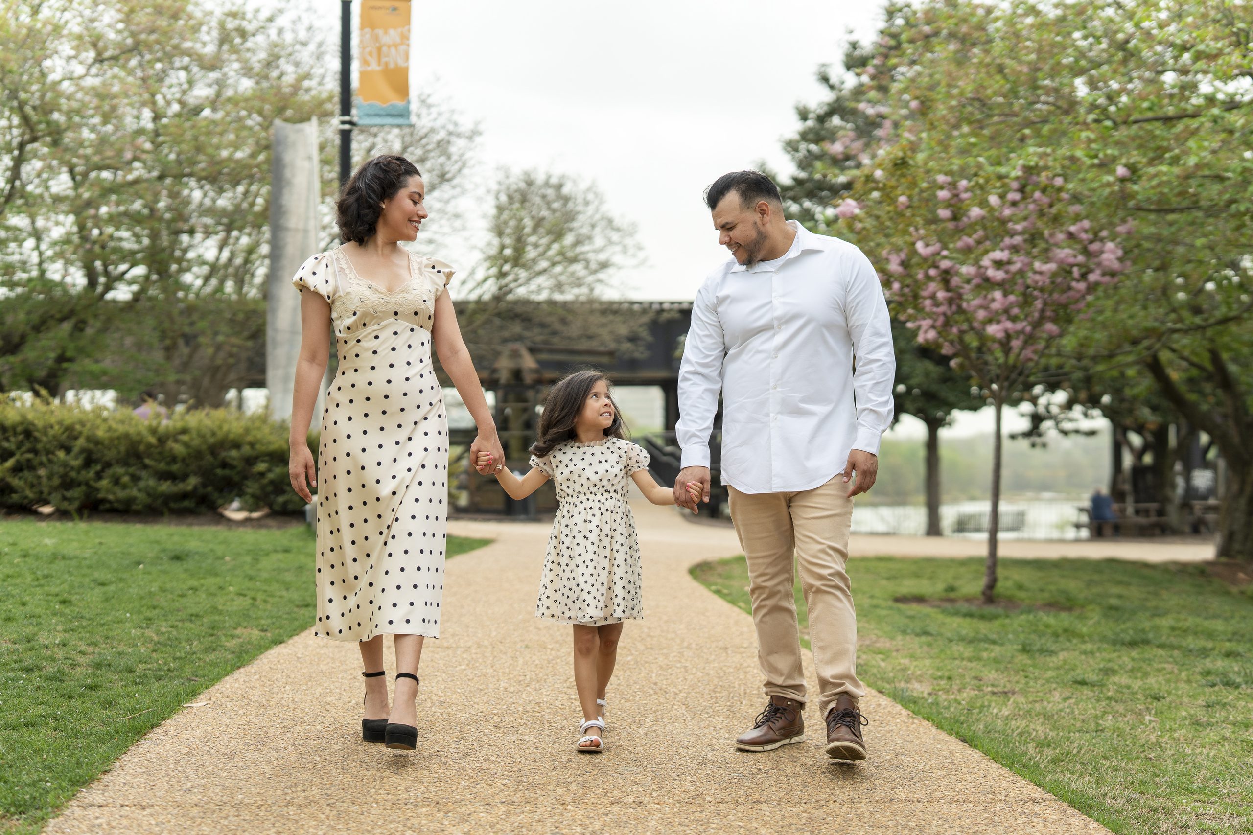 Parents walking hand in hand with their daughter along a blossom-lined path