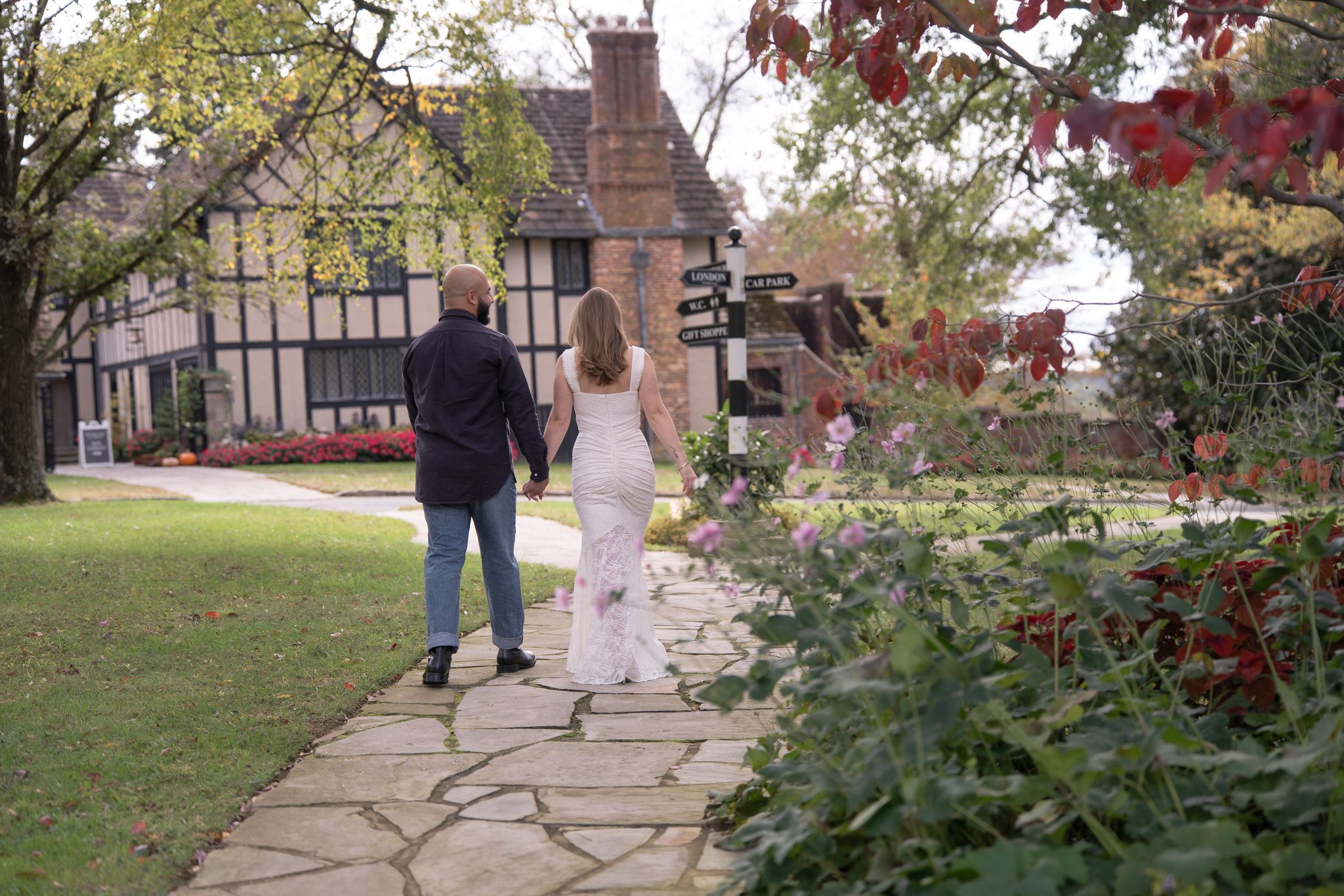 Couple walking a stone path toward the Tudor manor at Agecroft Hall, framed by red autumn leaves